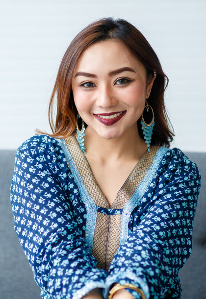 Jovem, linda menina asiática bonito, vestido em estilo cigano casualmente roupas com auto-confiante maneira, sentado no sofá e olhando para a câmera. - Foto, Imagem