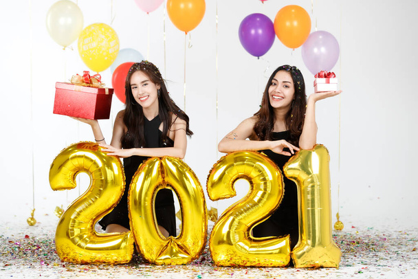 Two young and beautiful sexy Asian girls holding golden numeric 2021  balloons with funds and happiness. Idea for new year celebrate party. - Фото, изображение