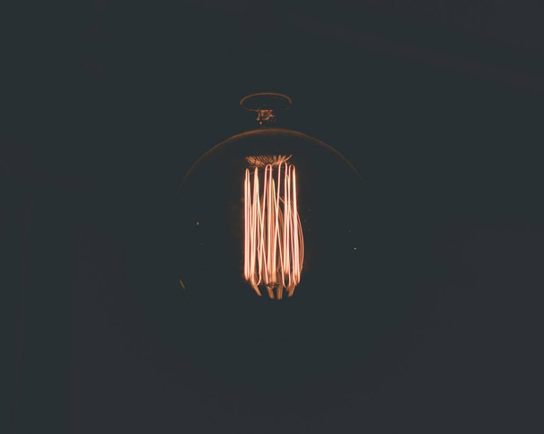 A closeup of the light bulb filament glowing in the darkness. - Zdjęcie, obraz