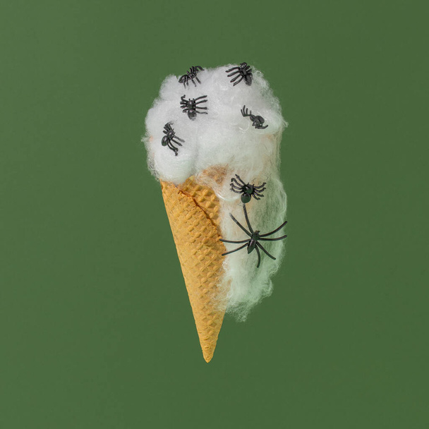 Ice cream cone with spider web and spiders on a green background. Spooky Halloween concept. - Photo, Image