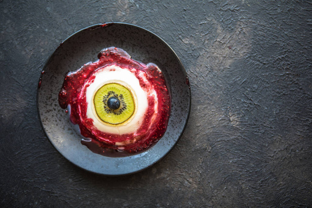 Halloween dessert bloederige oog van vanille panna cotta en kiwi met bessensiroop - Foto, afbeelding