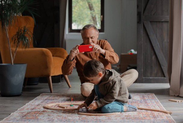 grandfather take a picture as grandson play with train at home - Foto, immagini