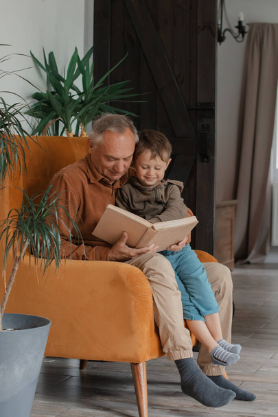 Ο παππούς διάβαζε ένα βιβλίο με τον εγγονό του στο σπίτι - Φωτογραφία, εικόνα