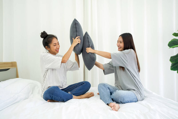 Δύο Ασιάτισσες έφηβες που παίζουν μαξιλαροπόλεμο στο κρεβάτι. - Φωτογραφία, εικόνα