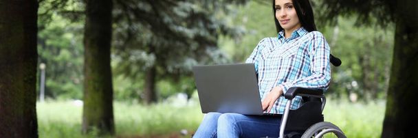 Fiatal nő tolószékben dolgozik laptop a parkban - Fotó, kép