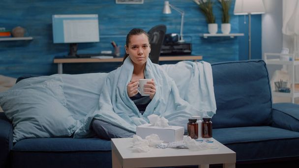 Egy influenzás nő portréja, aki egy csésze teát tart a takaróban. - Fotó, kép