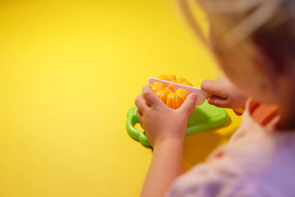 A child cuts a toy pepper on a yellow background with a toy knife - Foto, Imagen