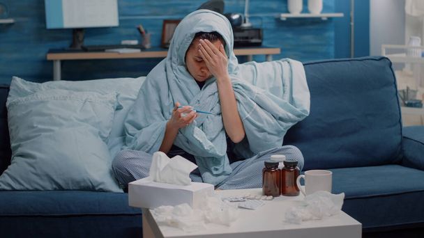 Nemocná žena pokrývající s dekou a při pohledu na teploměr - Fotografie, Obrázek