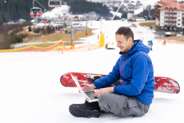 snowboarder masculino usando el ordenador portátil en paisaje nevado de la montaña - Foto, imagen