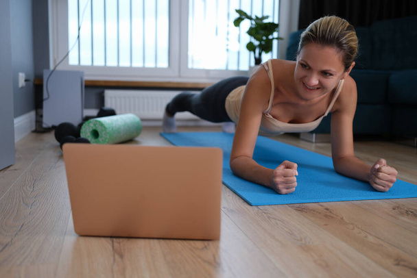 Giovane donna sana che fa esercizi di tavola a casa mentre guarda una sessione di allenamento online dal computer portatile - Foto, immagini