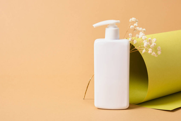 flower and mock up blank white bottle with dispenser for cosmetics on the background of a roll of green paper texture, natural cosmetics concept - Valokuva, kuva