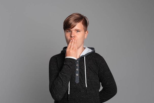 Oops emotion. Teen boy cover mouth with hand, looks at camera, stands over grey background, wearing in casual clothes. Expressive facial expressions - Photo, Image