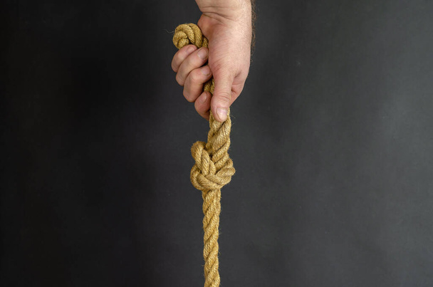 Erwachsene Männer halten senkrecht ein Seil mit einem Knoten. Hand hält ein Geläut - Foto, Bild
