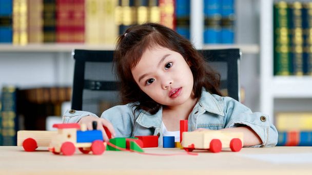 Lovely little Asian girl cieszyć się zabawką i kolorowe drewniane bloki i skoncentrować się na stos każdej warstwy wysokiej jako edukacji struktury i równowagi umiejętności siedząc na biurku do nauki w domu biblioteki - Zdjęcie, obraz