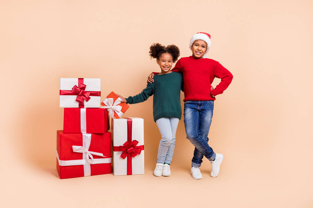 Photo of two adopted kids hug each other receive gifts wear x-mas hat jumper isolated beige color background - Foto, Bild