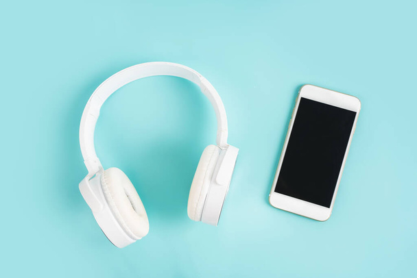 Mobile phone with blank screen and white headphones on a blue table top view - 写真・画像