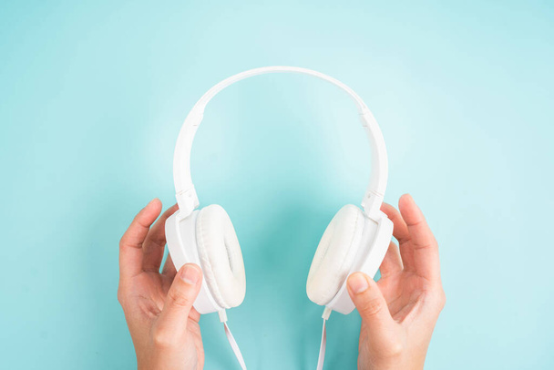 Female hands holding white headphones on blue background. - Foto, imagen