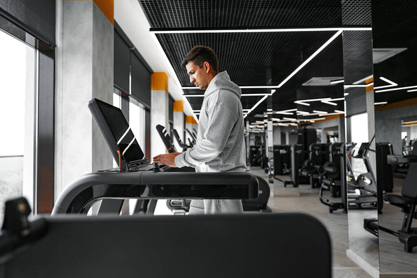 Portrait of a young man in orange windbreaker workout on a fitness machine at gym. - Foto, afbeelding