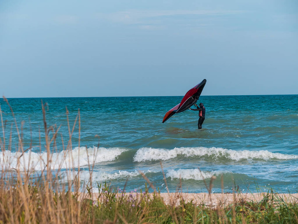 Спортсмен катается на доске для серфинга с помощью ручного крыла фольги на океанских волнах. Осенний экстремальный спорт. Осенний отдых на море. Ветреная погода на пляже. - Фото, изображение