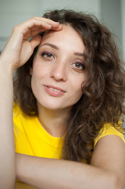 Beautiful curly girl in yellow t-shirt is looking at the camera at home in her apartment, posing with smile, happy people concept - Photo, Image