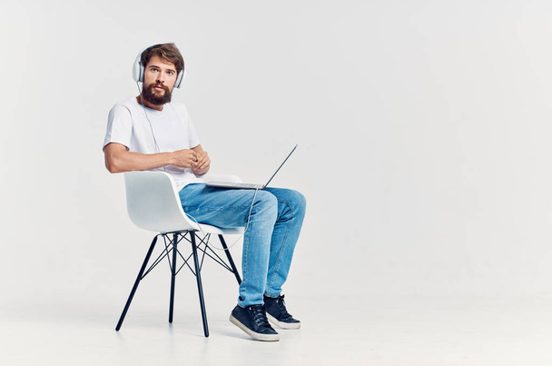 άνδρας με λευκό t-shirt κάθεται σε μια καρέκλα με ένα φορητό υπολογιστή στην ψυχαγωγία ακουστικά - Φωτογραφία, εικόνα