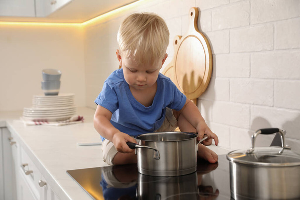 Curious little boy playing with pot on electric stove in kitchen - Photo, Image