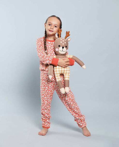 Cute girl in pajamas with toy deer on light grey background - Foto, Imagen
