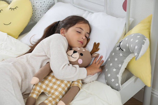 Cute girl in pajamas sleeping with toy deer at home - 写真・画像