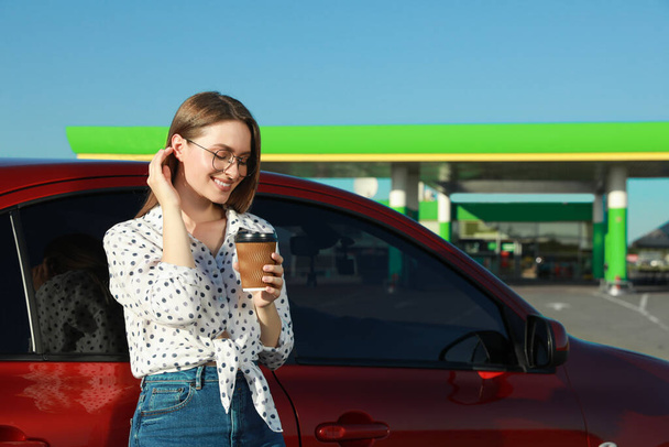 Beautiful young woman with coffee near car at gas station - Фото, зображення
