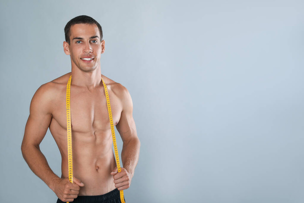 Handsome shirtless man with slim body and measuring tape on grey background. Space for text - Foto, immagini