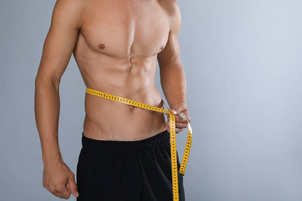 Shirtless man with slim body and measuring tape around his waist on grey background, closeup. Space for text - Foto, Bild