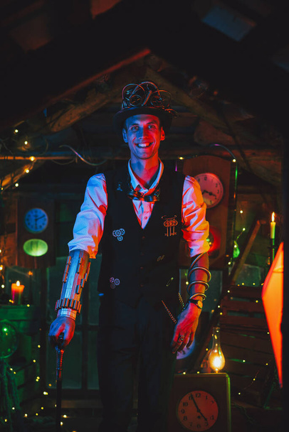 inventor masculino feliz em um terno steampunk, chapéu superior, óculos e com um sorriso de cana em uma oficina de relógio - Foto, Imagem