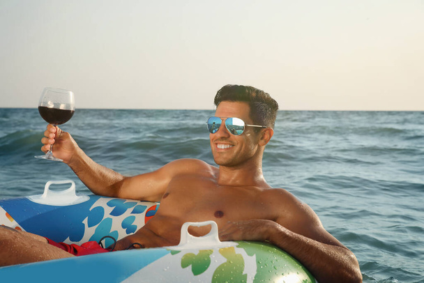 Man with glass of wine and inflatable ring resting in sea - Foto, immagini