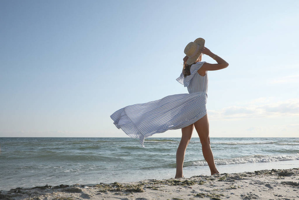 Woman in dress with straw hat walking by sea on sunny day - Foto, Imagen