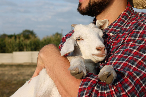 Farmer with cute goatling outdoors, closeup. Baby animal - Fotó, kép