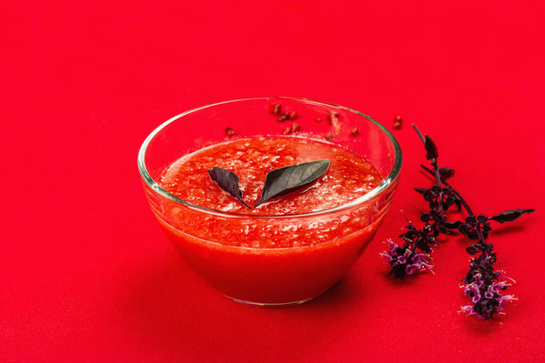 Домашний томатный суп. Здоровая вегетарианская еда, минималистичная концепция. Розовый перец, фиолетовый базилик. Ярко-красный матовый фон, пространство для копирования - Фото, изображение