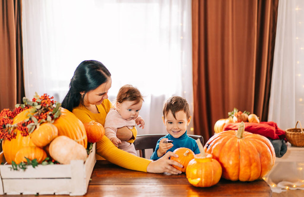 A happy family is getting ready for Halloween. a beautiful young mother and her two children are carving pumpkins at home - Foto, afbeelding