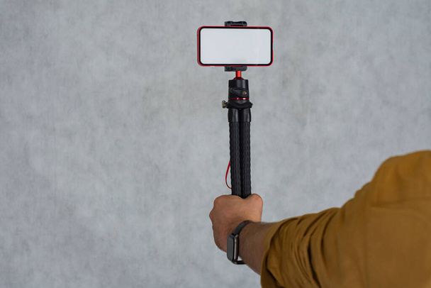 A man holds a flexible tripod with a mock-up of a smartphone with a white screen - Фото, зображення