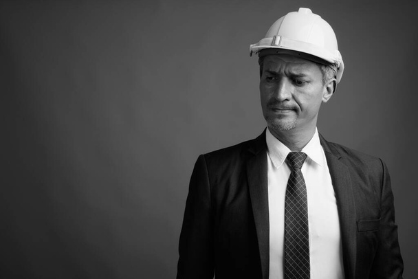 Studioaufnahme eines Geschäftsmannes mit Hut vor grauem Hintergrund in Schwarz-Weiß - Foto, Bild