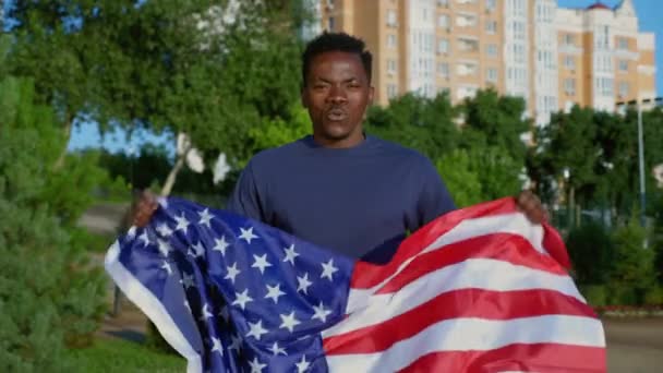 Портрет улыбающийся афроамериканец с американским флагом, смотрит в камеру говорит США - Кадры, видео