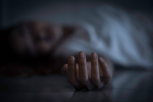 Крупним планом рука мертвого тіла азіатки вдома. Розмита дівчина в білій сорочці лежить на підлозі з темним тоном
 - Фото, зображення