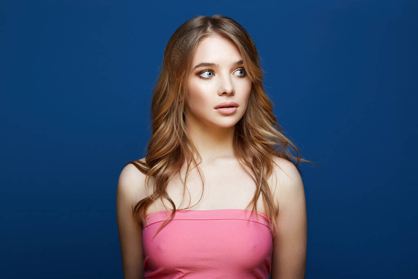Beautiful young woman in pink dress over blue background. blond girl with makeup - Fotografie, Obrázek