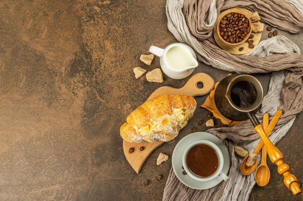 コーヒーとクロワッサン、朝と朝食のコンセプト。コーヒー、ミルクジャグ、コーヒー豆と銅ターク。茶色の石のコンクリートの背景、トップビュー - 写真・画像