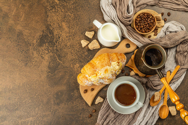Kaffee und Croissant, Guten Morgen und Frühstück. Kupfertürke mit Kaffee, Milchkanne, Kaffeebohnen. Brauner Stein Beton Hintergrund, Draufsicht - Foto, Bild
