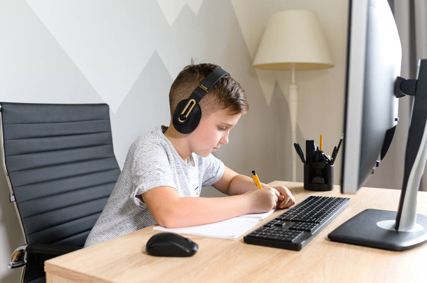 Schooler boy wearing headphones is studying in front of the computer - Photo, image
