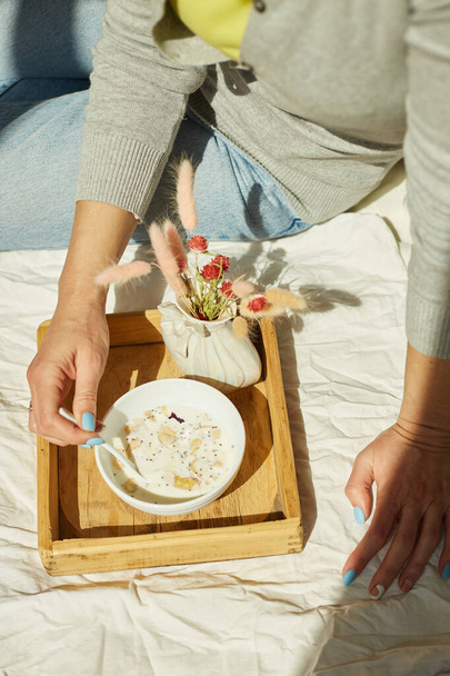 Woman in jeans sitting on the bed, and eating healthy granola bowl during the morning sunlight, breakfast in the bed. - Foto, immagini