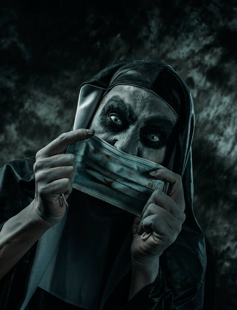 Крупный план страшной злой монахини, в типичной черно-белой привычке, надевающей или снимающей грязную одноразовую маску - Фото, изображение