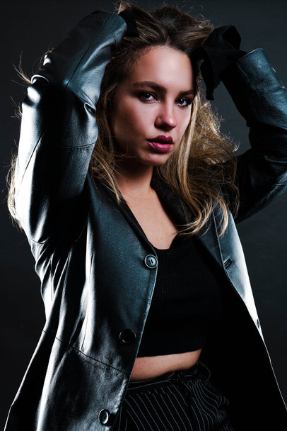 beautiful young woman in black leather jacket and sunglasses posing on grey background - Zdjęcie, obraz