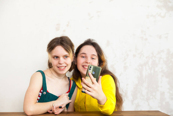 Две девочки-подростки сидят за столом и смотрят видео на смартфоне.  - Фото, изображение