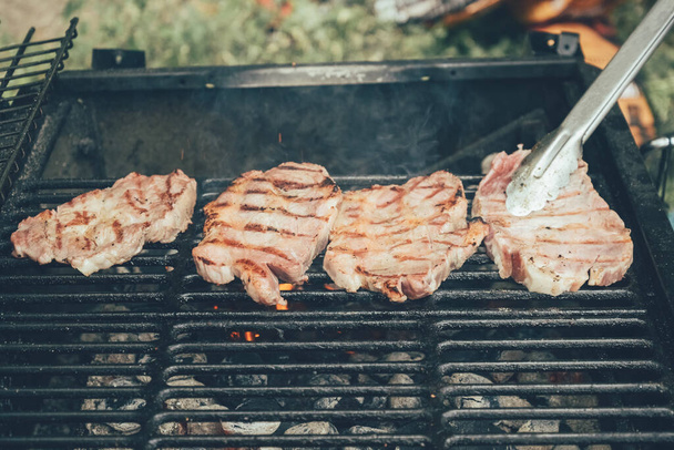 Grilled pork steaks. The cook turns the steak over with tongs. - 写真・画像